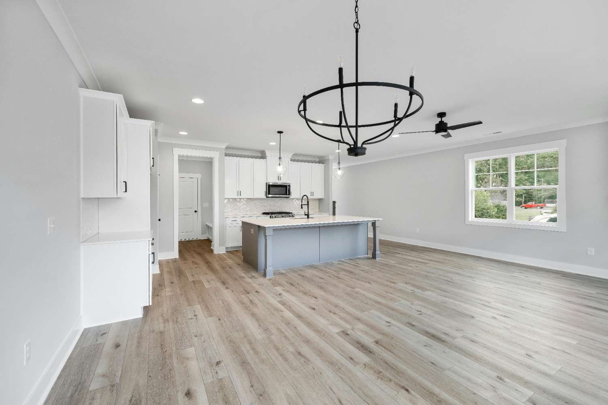 pen kitchen and living room with light grey oak laminate wood flooring, white cabinets, central island, black chandelier, ceiling fan, and large window.