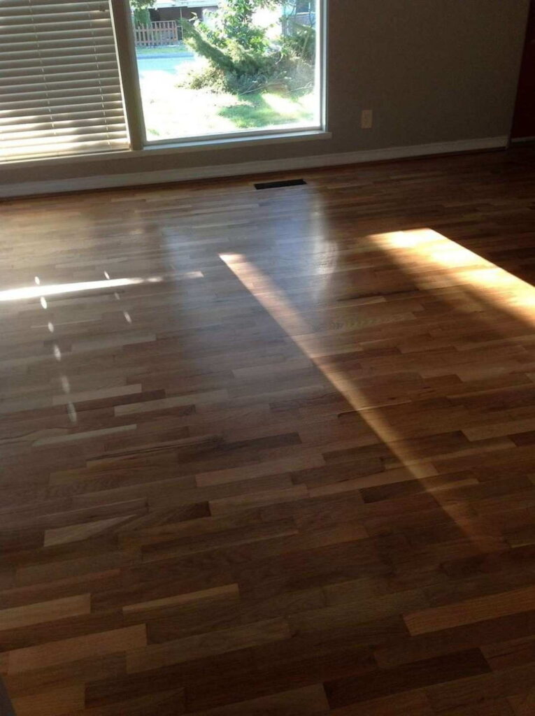 Empty room with natural light highlighting engineered wooden flooring near a large window.