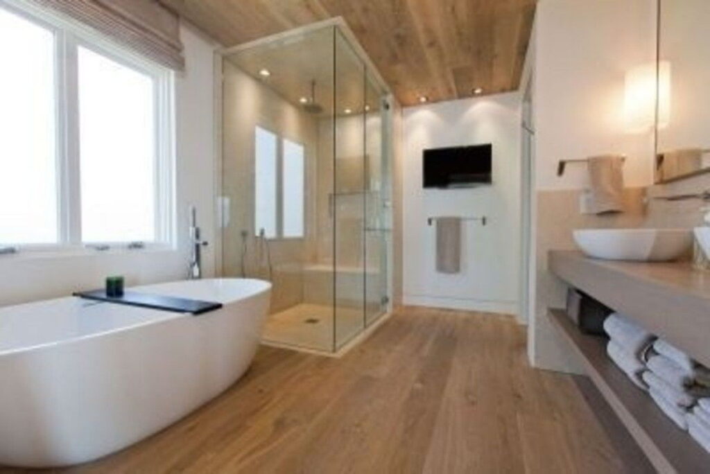 Modern bathroom with freestanding bathtub, glass shower enclosure, and engineered wooden flooring.