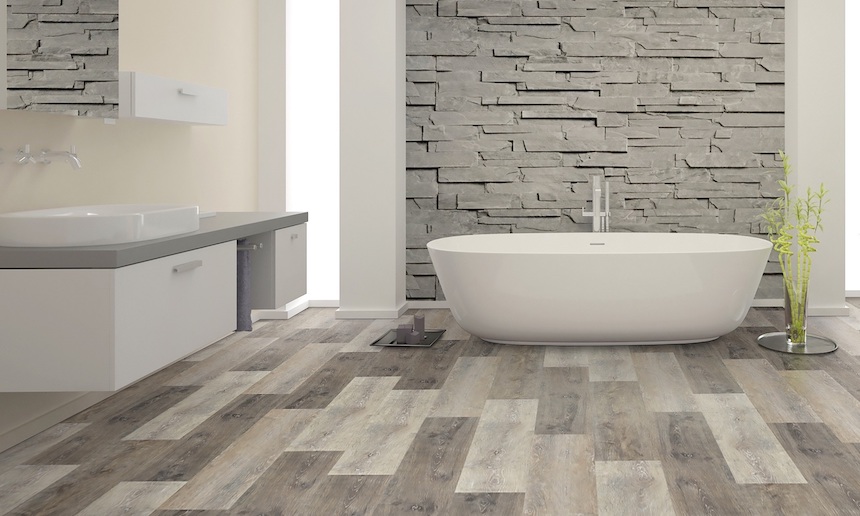 Modern bathroom with freestanding bathtub, stone accent wall, and grey wood-look luxury vinyl flooring installation.