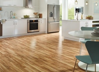Kitchen interior with light oak laminate wood flooring, white cabinets, stainless steel appliances, and dining table with modern chairs.
