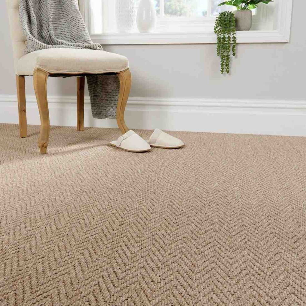Beige carpet with herringbone pattern in a cozy room with chair, slippers, and throw blanket