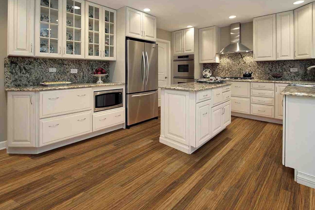 Modern kitchen with white cabinets, stainless steel appliances, granite countertops, and warm wood-look luxury vinyl flooring installation.